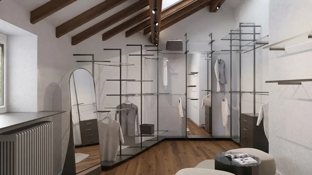 Attic dressing room under exposed dark wood roof beams with a freestanding black metal rail and glass shelf system, an arched floor mirror, a low drawer unit and a white radiator under the window