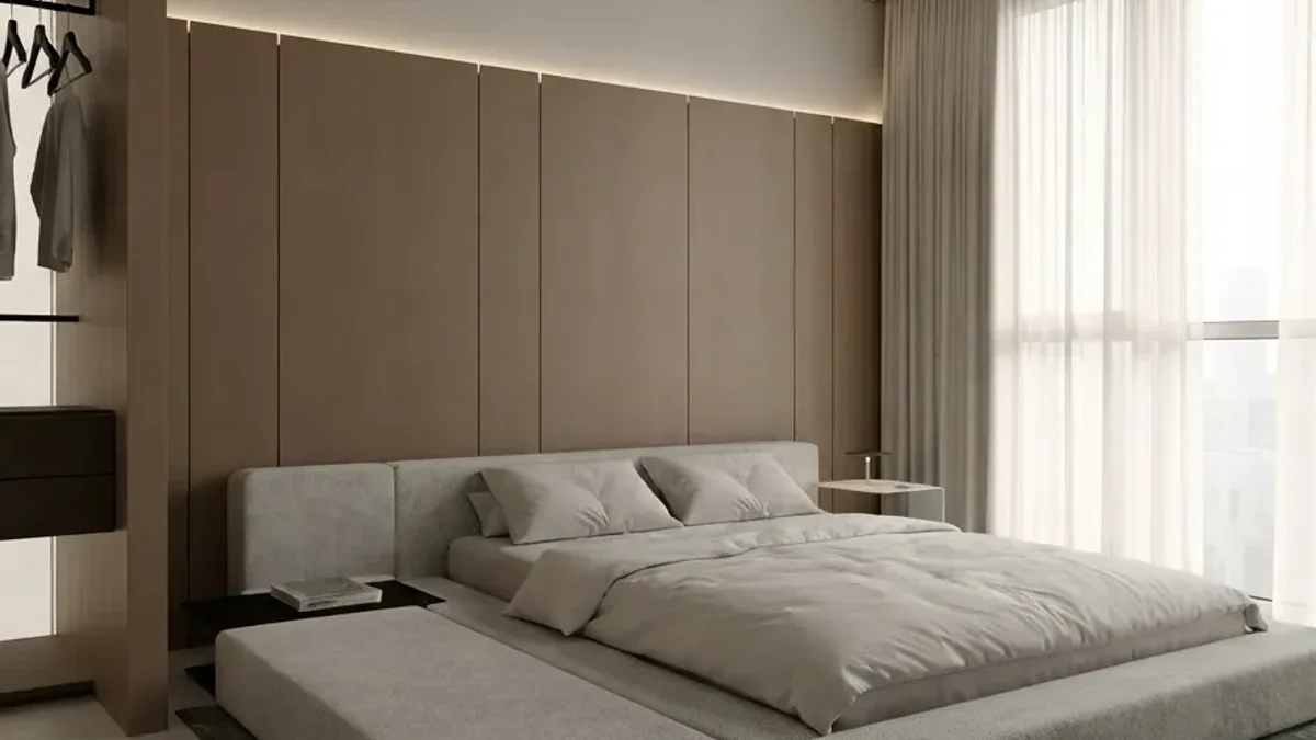 Minimal bedroom with a full-height wall of flush oak wardrobe doors with no visible handles behind a low upholstered bed, with sheer curtains on the window