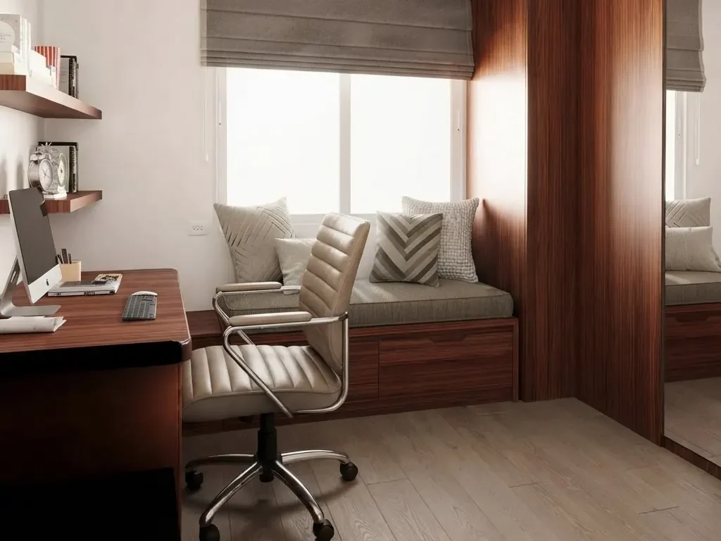 A small home office with a rosewood desk along the side wall, perpendicular to the window, a leather office chair with room to roll back, and a cushioned window seat under the window