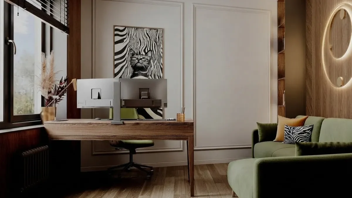 Home office with a walnut desk set at a right angle to the window, two monitors, a green velvet sofa against the opposite wall, paneled cream walls and a backlit round wall light