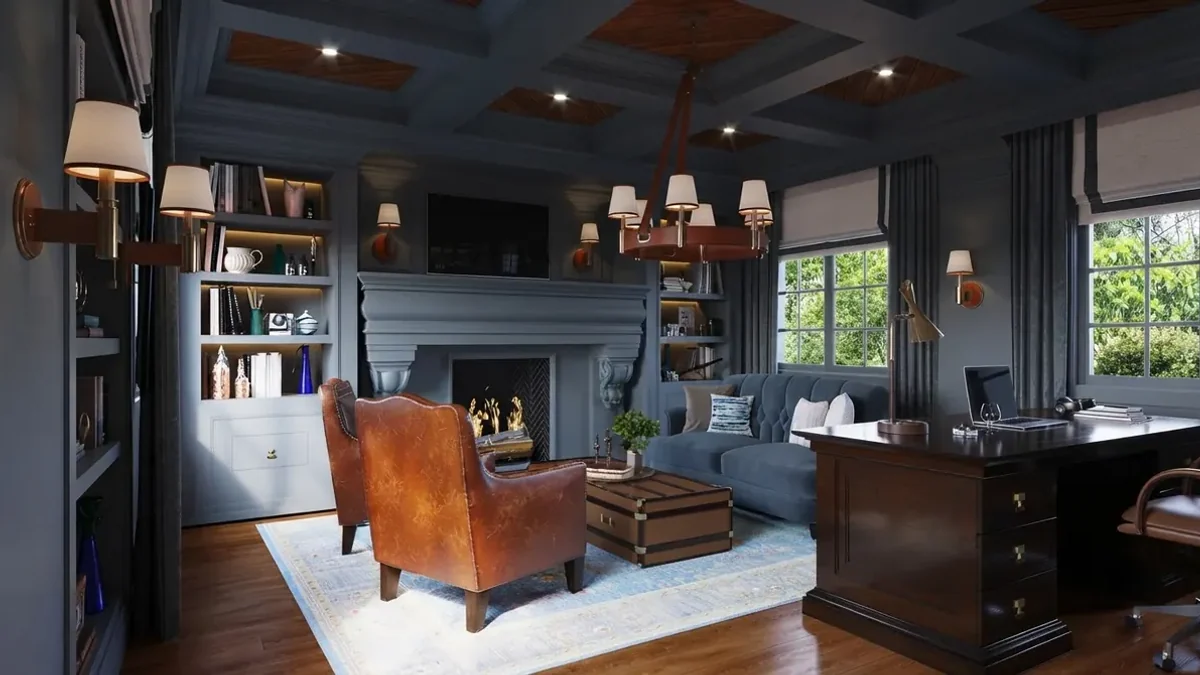 Dark academia home office in slate blue: coffered ceiling, built-in bookcases around a painted fireplace, two worn leather armchairs, a blue tufted sofa and a dark mahogany pedestal desk under shaded wall sconces