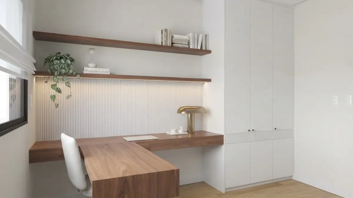Small white home office with an L-shaped floating walnut desk, two walnut shelves above a fluted panel with LED strip light, a brass mushroom lamp, a white chair and full height white wardrobes