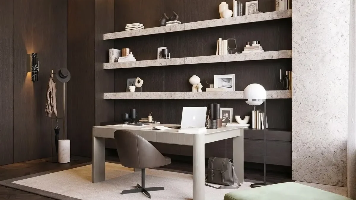 Dark walnut paneled home office with three long travertine floating shelves, a pale gray desk with a laptop, a brown leather task chair, a globe floor lamp and a cream rug