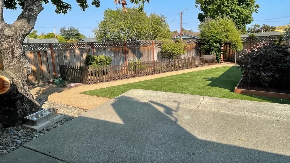 The base backyard rendered as a dog-friendly yard with artificial turf, a perimeter gravel path, a fenced bed and a shaded water station
