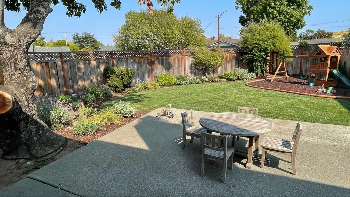 The base backyard rendered as a family yard with a central play lawn, a timber playhouse and swing on rubber mulch and a dining patio