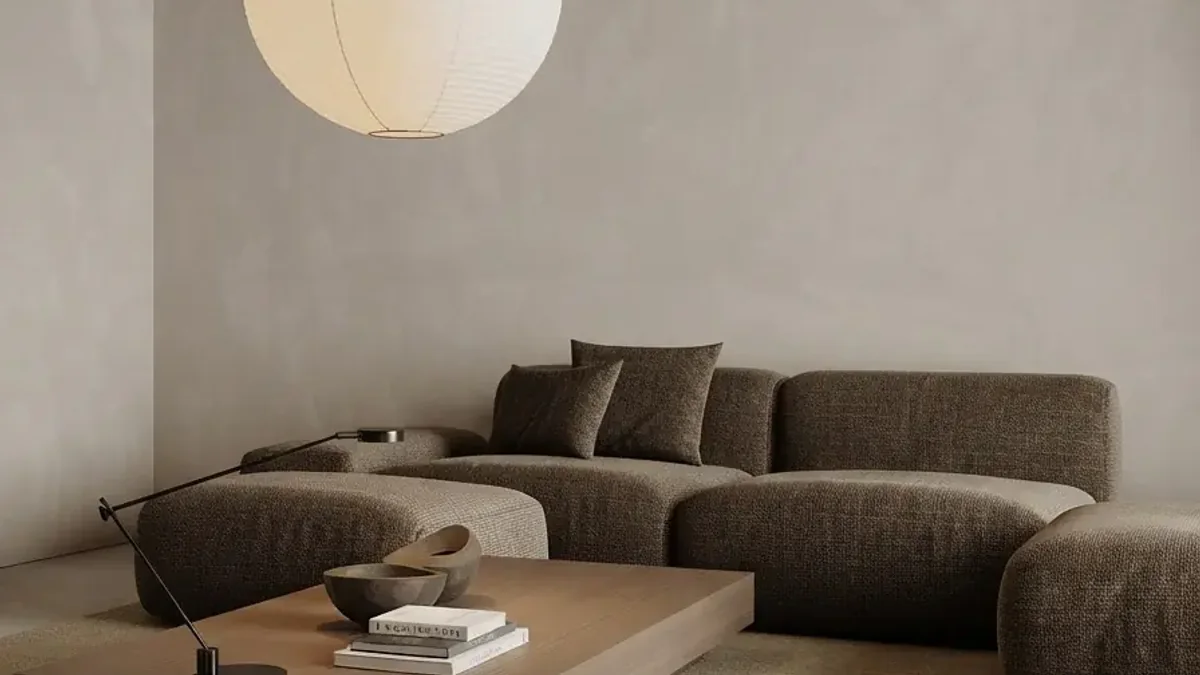 Very pale plaster living room with a large paper globe pendant, a brown grey boucle modular sofa with matching ottoman and a low pale wood platform table holding books, a bowl and a slim black task lamp
