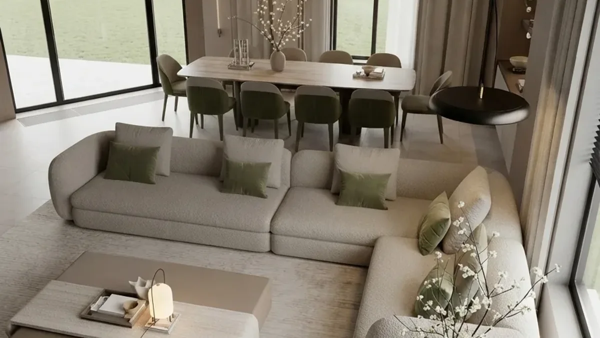 An open plan living and dining room with a cream corner sofa and olive cushions in the foreground, a low pale table, and a dining table with olive upholstered chairs under a linear light beside full height glazing
