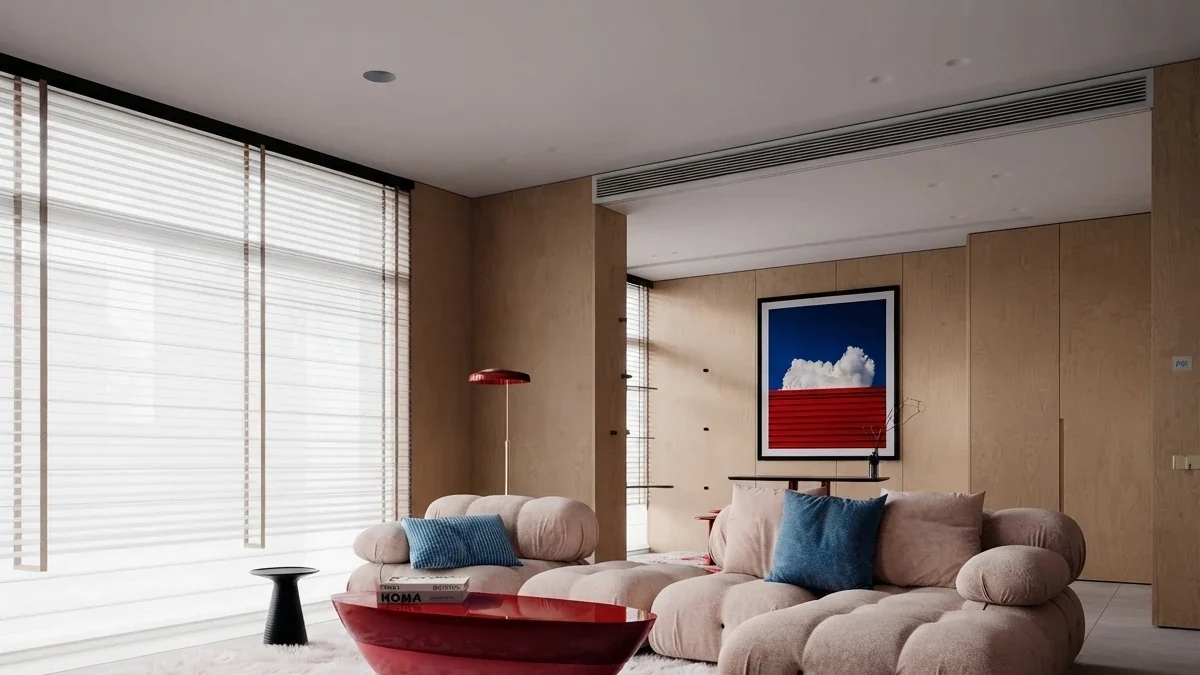 Bright apartment living room with a beige modular sofa, a red coffee table and one large square painting of a white cloud over a red horizon hung centred on a pale timber wall