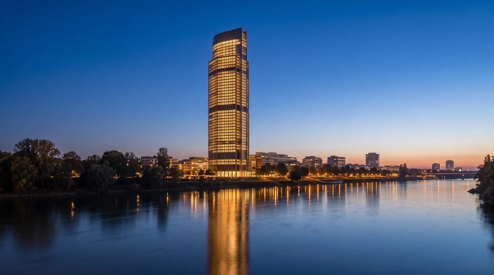 A photorealistic render of a 30 storey office tower at blue hour, every floor lit warm through the glass curtain wall, seen across water with the city behind