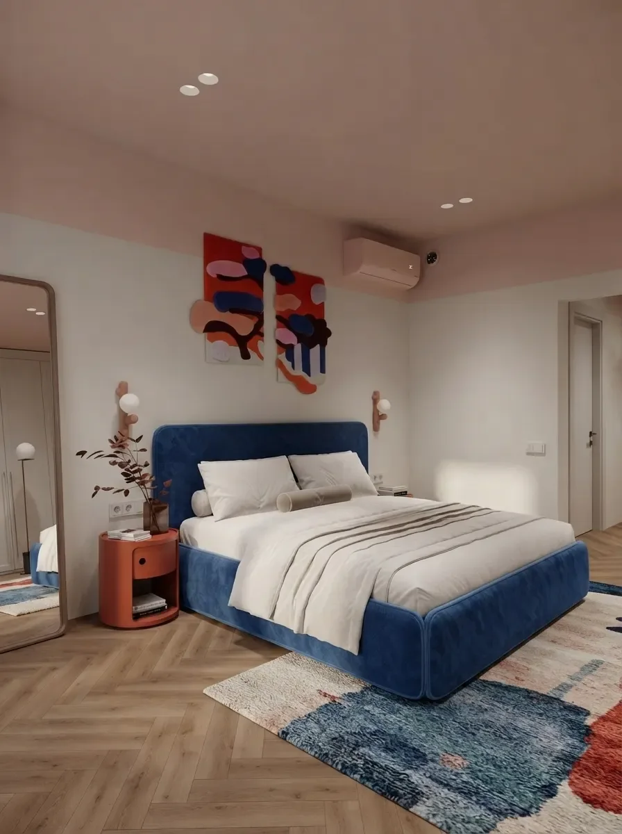 Small apartment bedroom render with a navy blue upholstered bed against a blush pink wall, one round red nightstand, colourful art above the headboard and a door on the right
