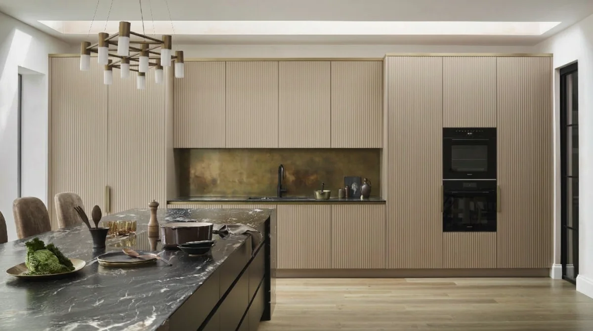Warm beige kitchen design with ribbed cabinet fronts, dark marble island countertop, brass accents, and oak hardwood flooring for a contemporary organic look