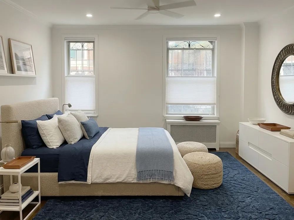 Bedroom redesigned into a calm coastal sanctuary with AI, upholstered bed with navy and white linens, deep blue textured rug, white dresser, round mirror, and layered lighting from a ChatGPT bedroom prompt visualized in MeltFlex
