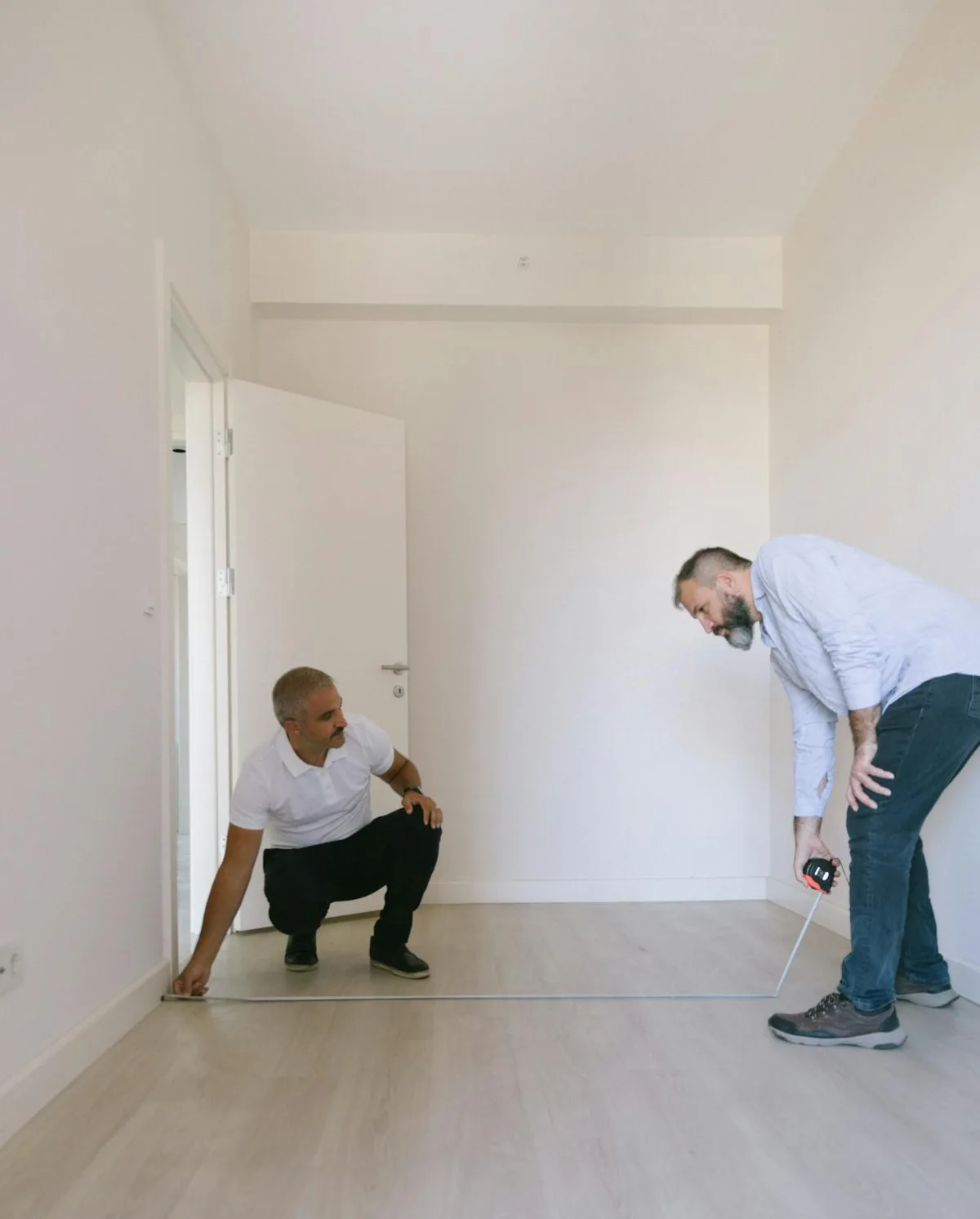 Person measuring a room floor with a tape measure before buying furniture
