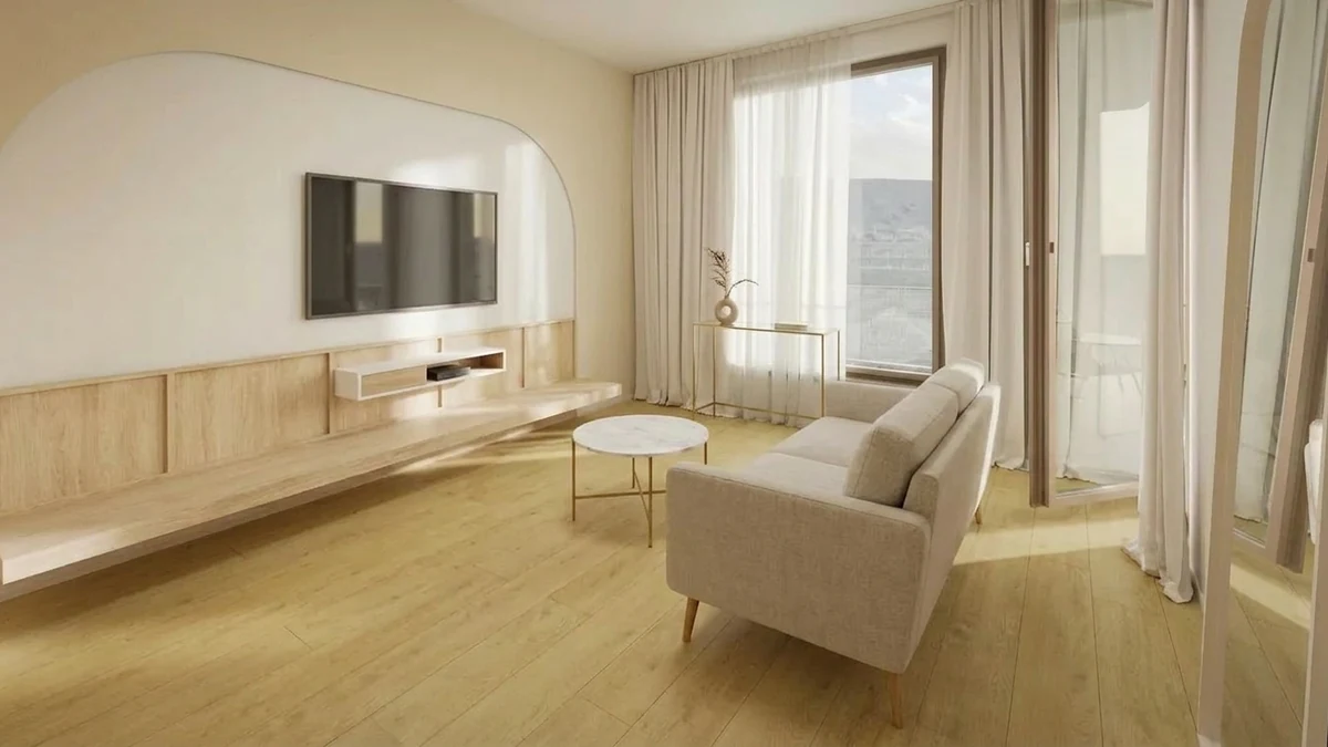 Small living room furnished correctly with a compact loveseat on legs, a small round coffee table and a wall-mounted TV, leaving plenty of visible floor and open walking space