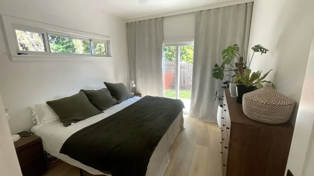 The finished bedroom in a converted garage unit, with a bed, high clerestory windows above head height, a sliding glass door to the garden and a timber chest of drawers