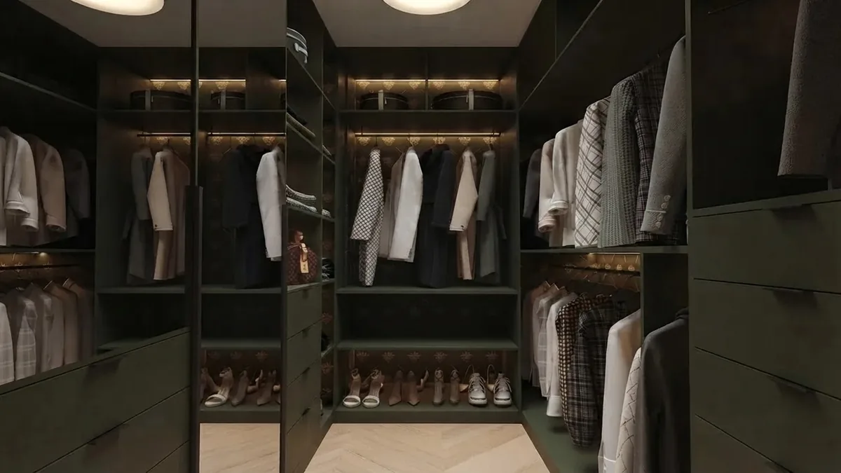 Dark green walk-in closet with double hung rods of shirts and jackets, a mirrored panel and a low shelf of heels and sneakers