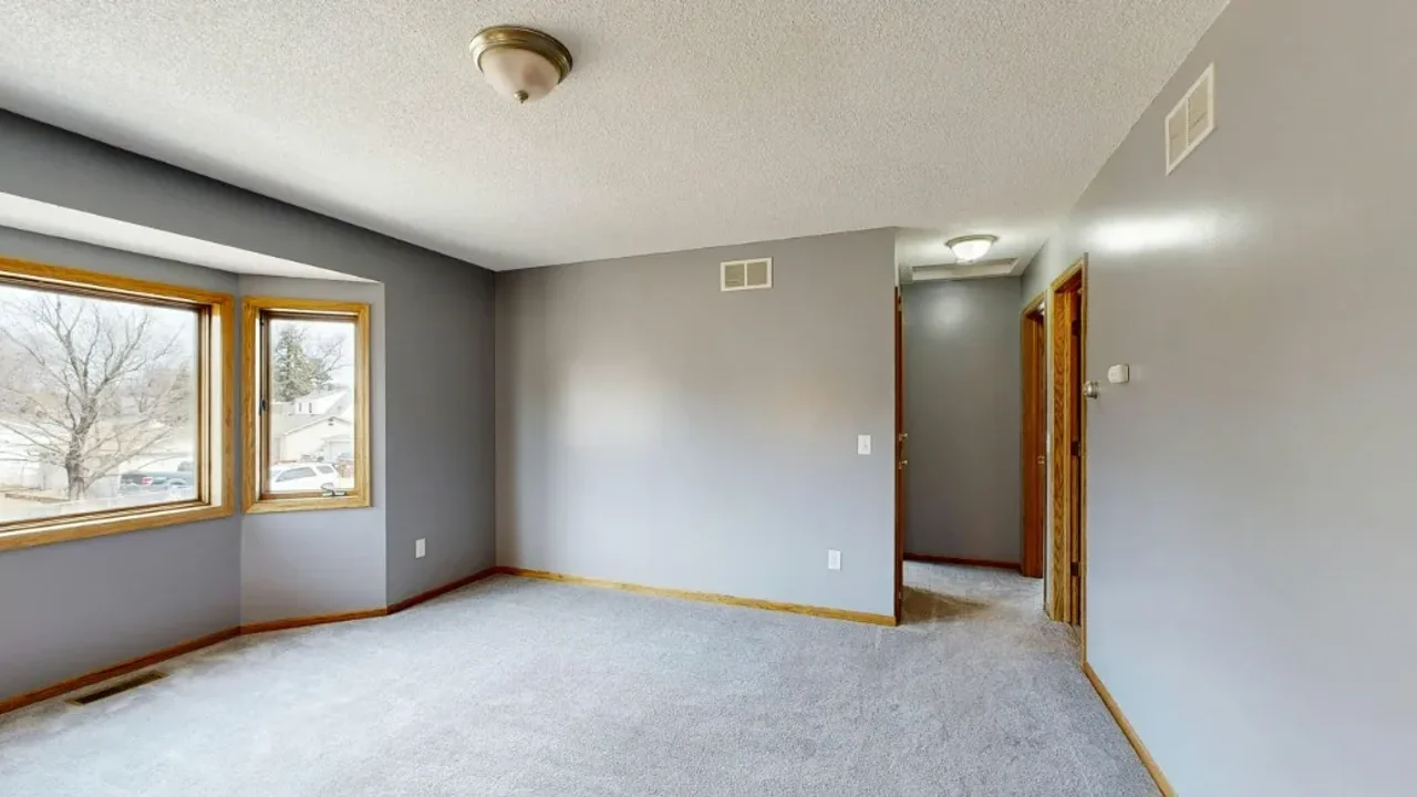 An empty, unfurnished living room with grey walls, a bay window and wood trim, the raw input photo before AI rendering