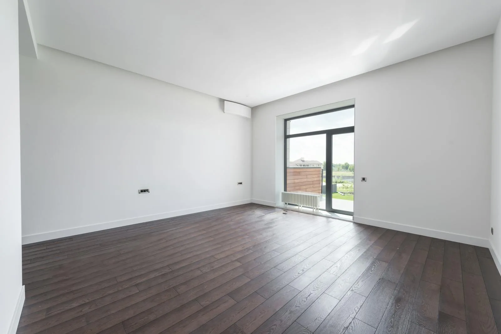 An empty, plain living room with bright daylight, wood floors and blank walls, the kind of bland space used as a before shot for AI interior design