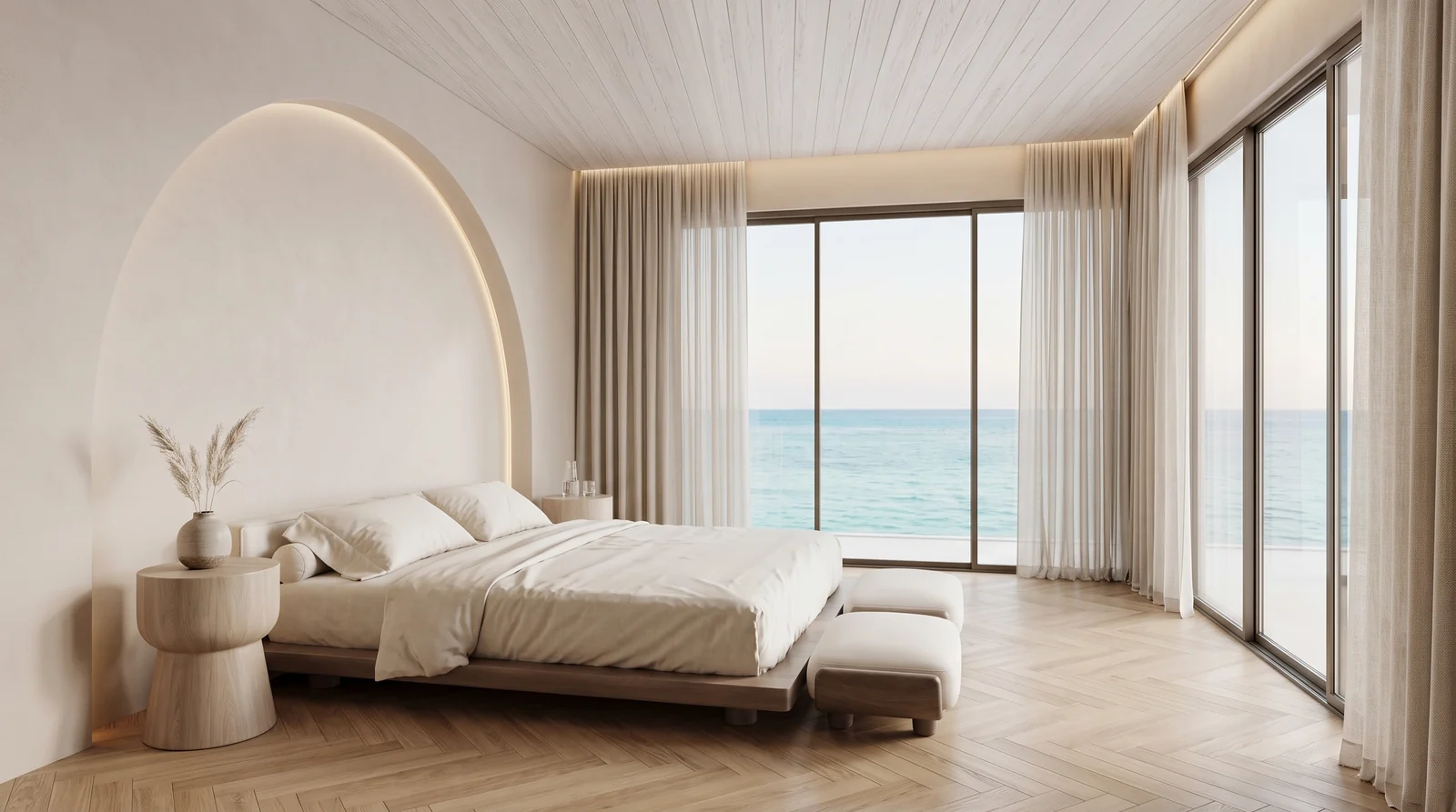 A primary bedroom with a low bed, an arched plaster headboard niche, oak herringbone floor and a sea view through full height glazing