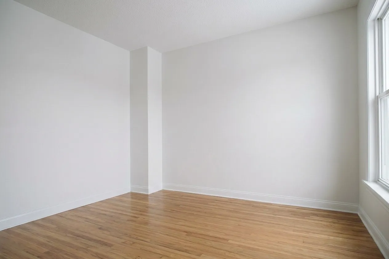 Empty room with light hardwood floors, white walls, window with natural light — blank canvas for nursery design