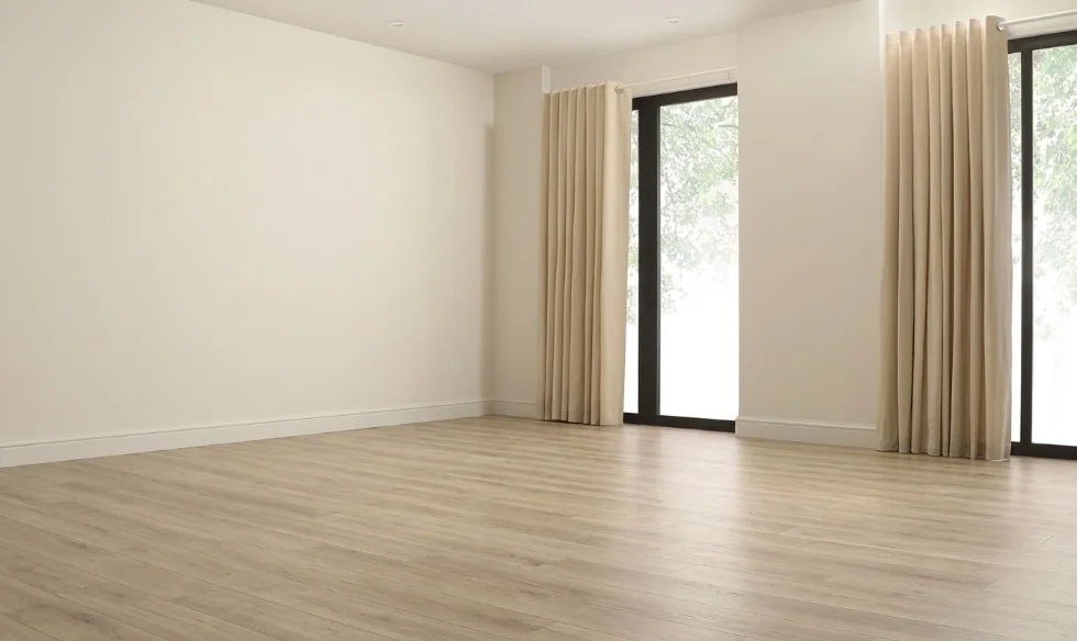 Empty modern apartment room with light wood floors, white walls, cream floor-to-ceiling curtains, and natural daylight from a large window