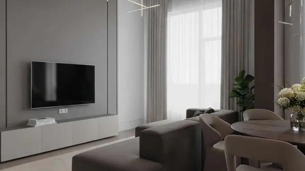 A grey and white living room with full height sheer curtains running the whole window wall, a wall mounted television on a pale low unit, a dark grey modular sofa, dining chairs to the right and a thin linear ceiling light
