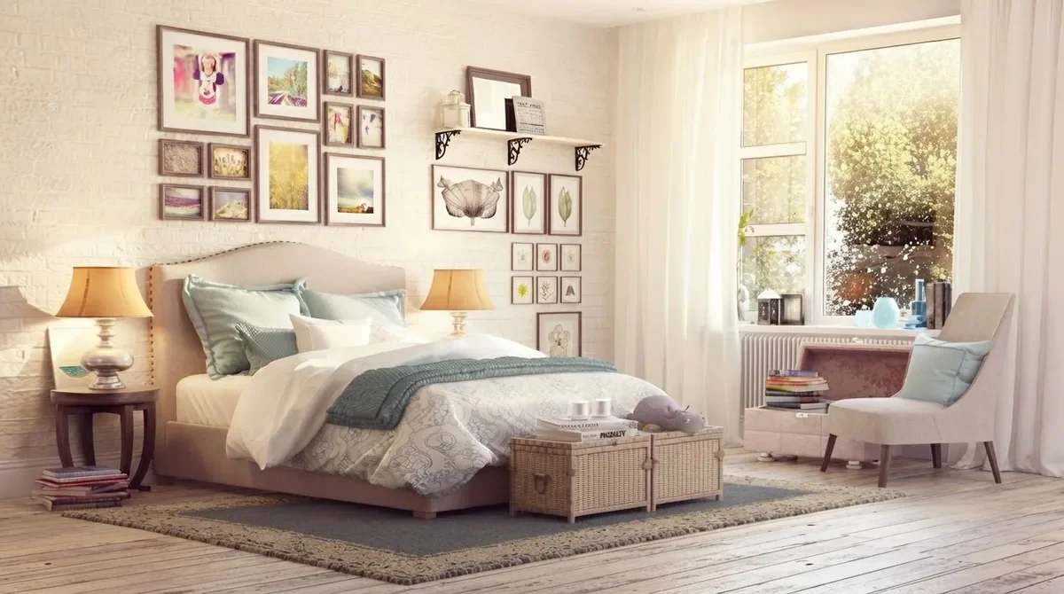 Bedroom with a gallery wall of botanical and floral prints and two bracket shelves above an upholstered bed, matching table lamps on both nightstands and a wicker trunk at the foot of the bed