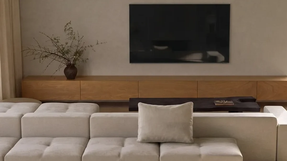 Warm minimal living room makeover result: a cream modular sofa against a full-width oak media wall with warm afternoon light
