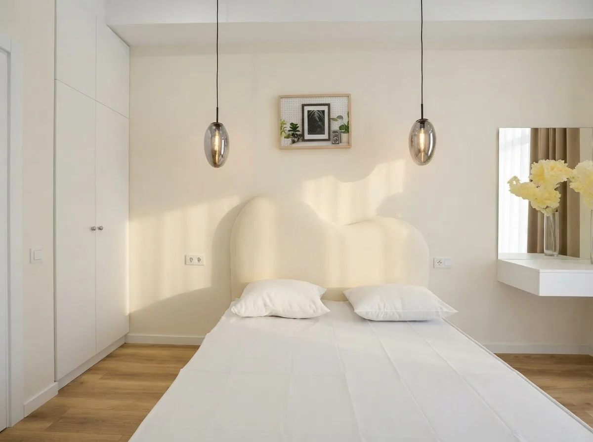 Real photograph of a bedroom with a curved white headboard, two pendant lights and a small artwork, walls in Alabaster