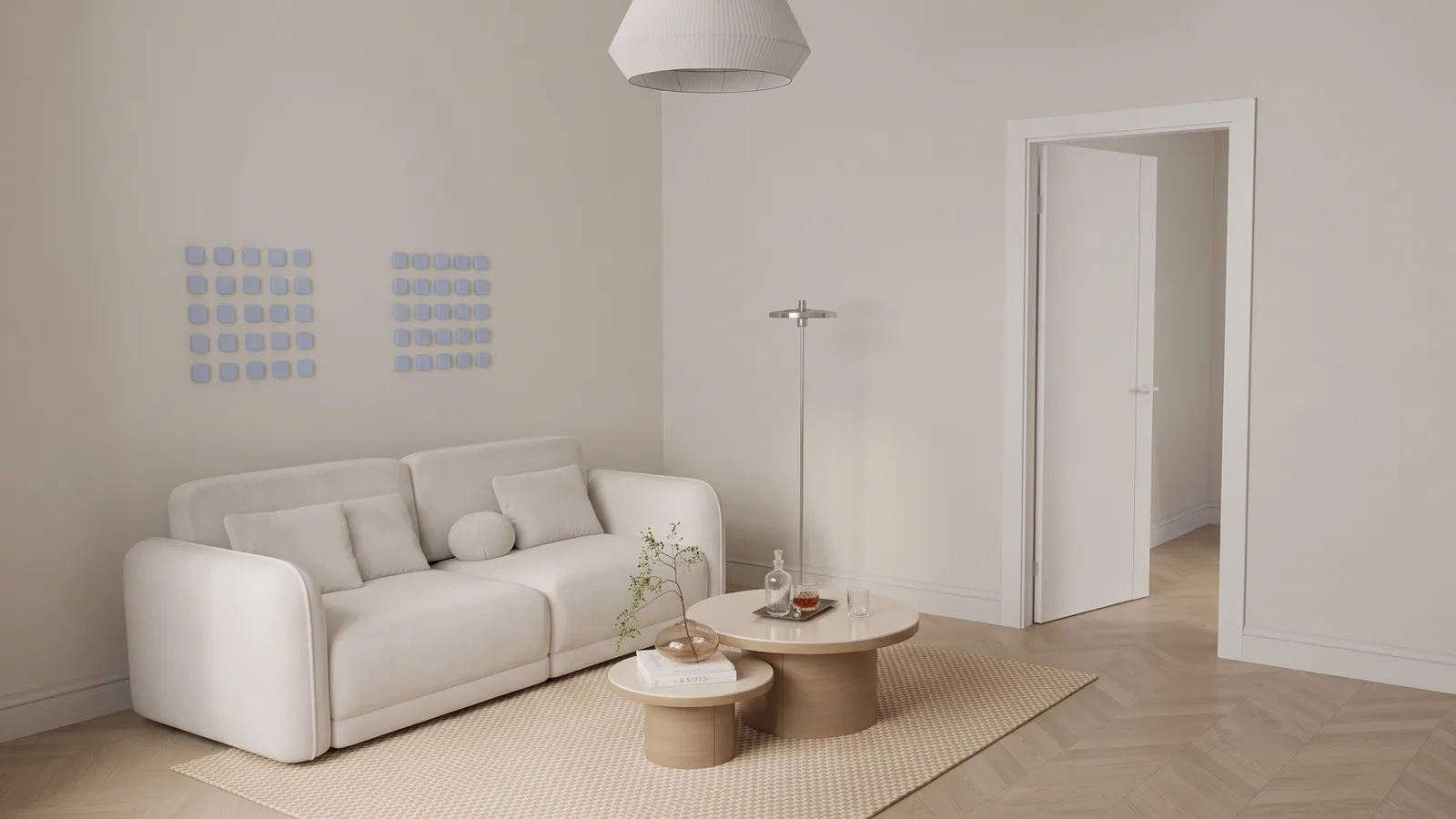 A cream two seat sofa with rounded arms in a bright apartment living room, an open white interior door to its right showing a pale hallway, nesting oak tables on a jute rug