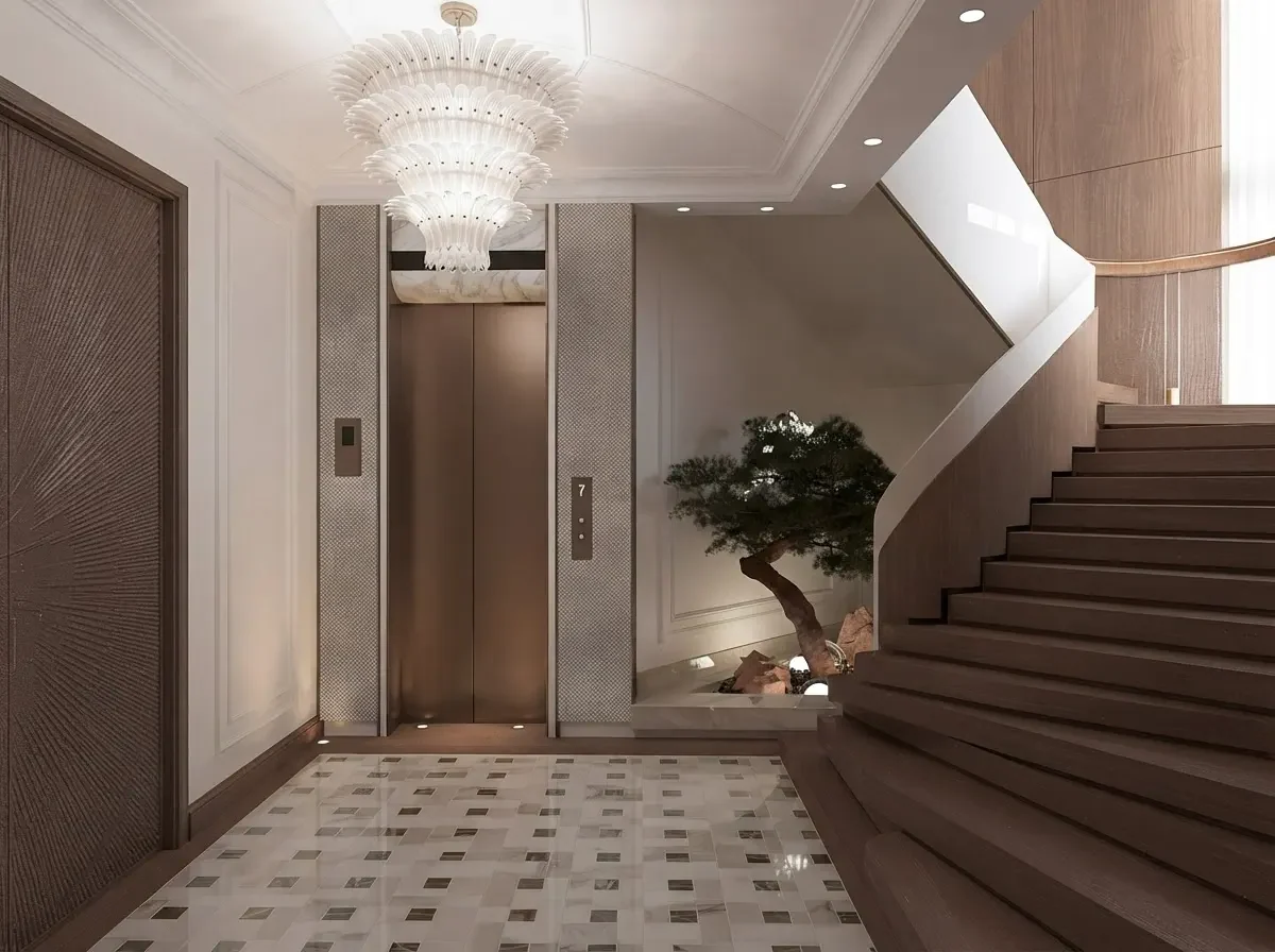 An entrance lobby with a chandelier, a lift, a patterned marble floor and a stone staircase rising on the right with a tree planted beneath it