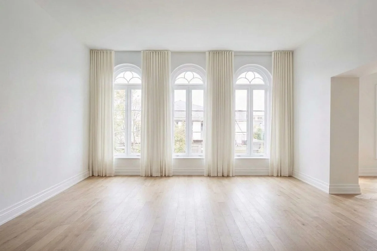 Same character home room with all furniture digitally removed showing three arched windows, cream curtains, white walls, and light wood herringbone floors