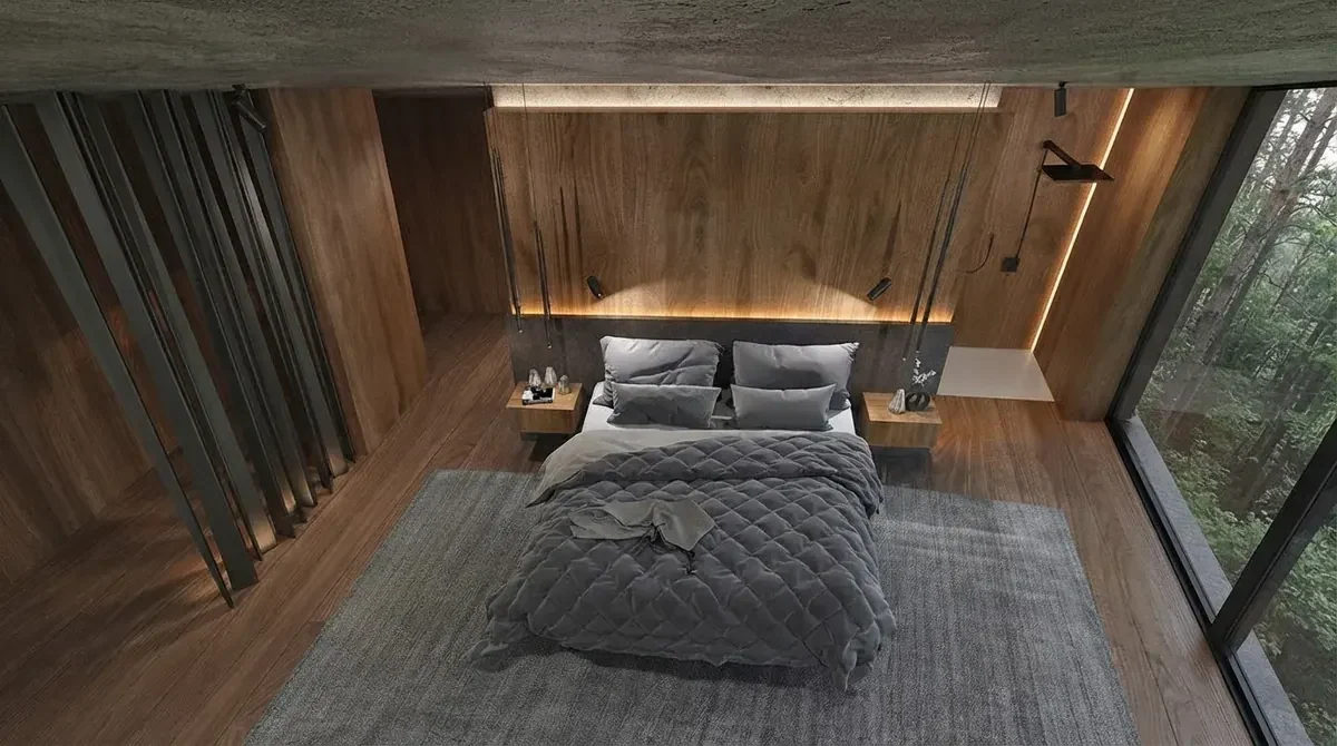 Timber and concrete bedroom with a grey quilted bed standing on a large charcoal rug that extends well past both sides and the foot of the bed