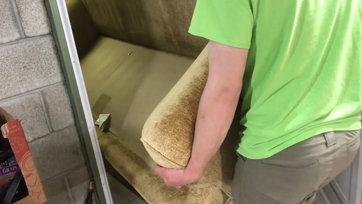 A mover carrying a full-size couch on its end through a tight doorway