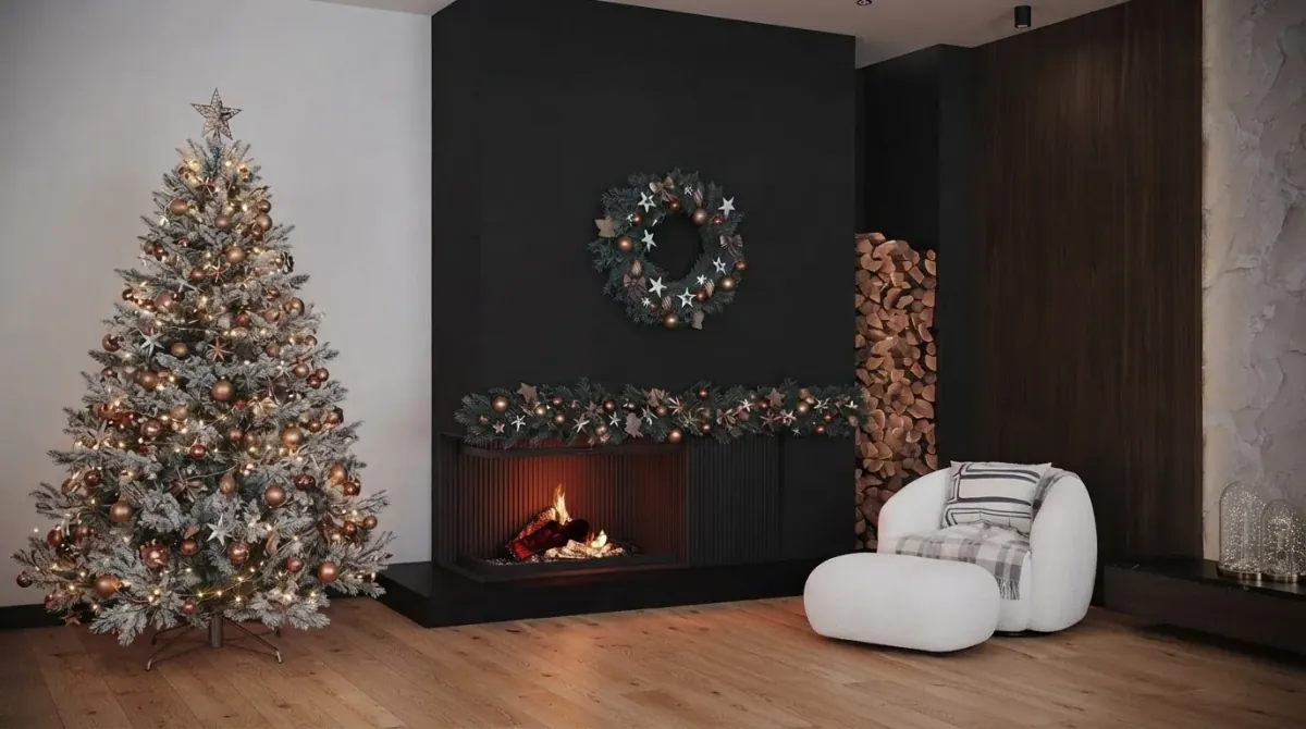 Chalet living room with a black fireplace wall, a wreath above the fire, a pine garland with lights along the hearth, stacked logs in a niche, a frosted Christmas tree with warm lights on the left and a white boucle armchair