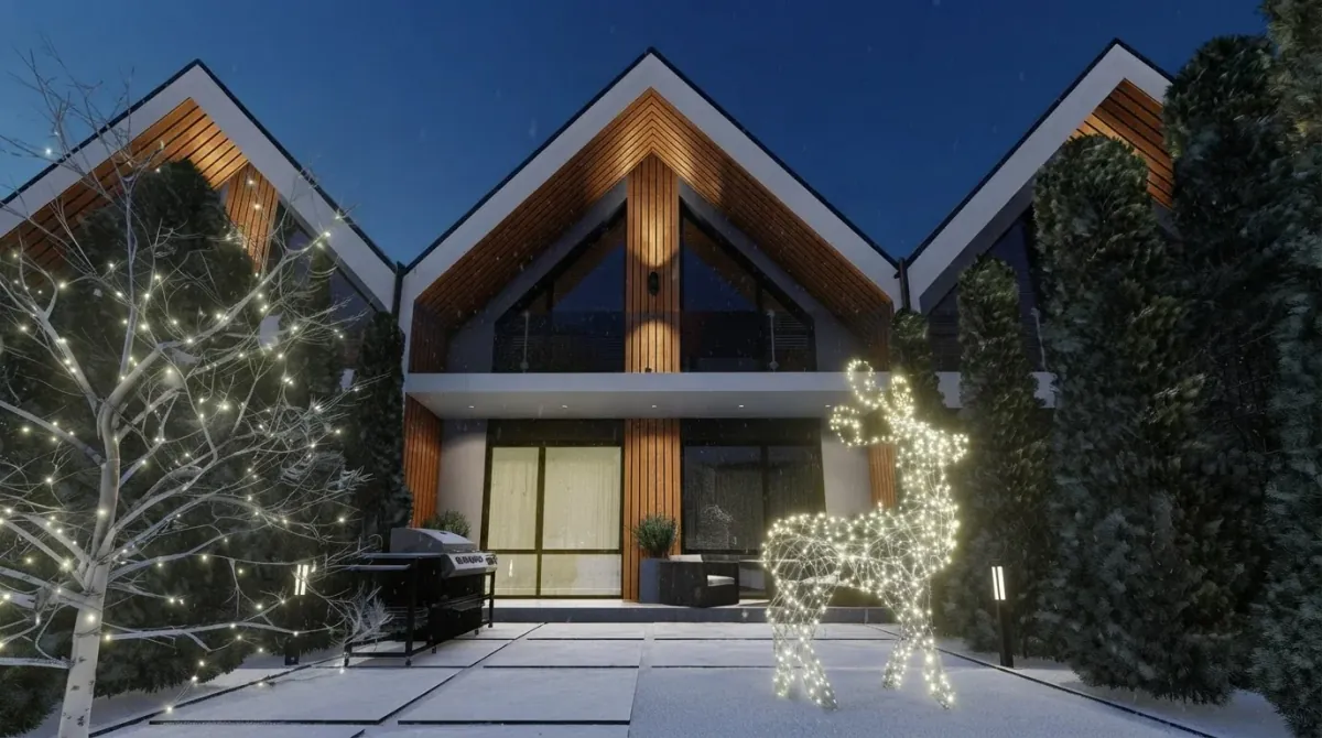 Gabled timber townhouses at dusk with a bare front garden tree wrapped in warm string lights and a lit wire reindeer beside the parked cars
