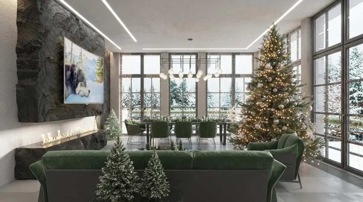 Open plan living and dining space with a tall lit Christmas tree standing between green velvet sofas and a long dining table, glass walls onto snow, a rough stone wall and small frosted trees on the coffee table
