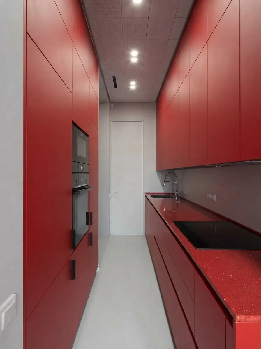 Narrow galley kitchen with high gloss red slab cabinet doors, tall red units around a built in oven and a dark countertop