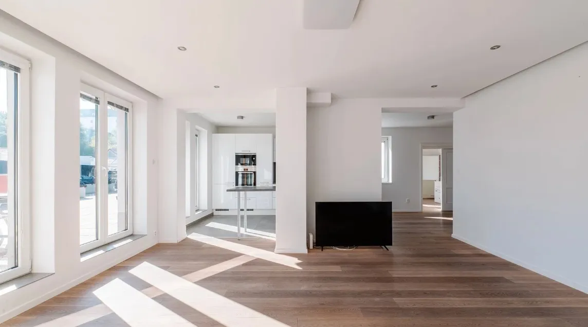 Empty open-plan living room with hardwood floors and large windows — the starting point before any furniture is added