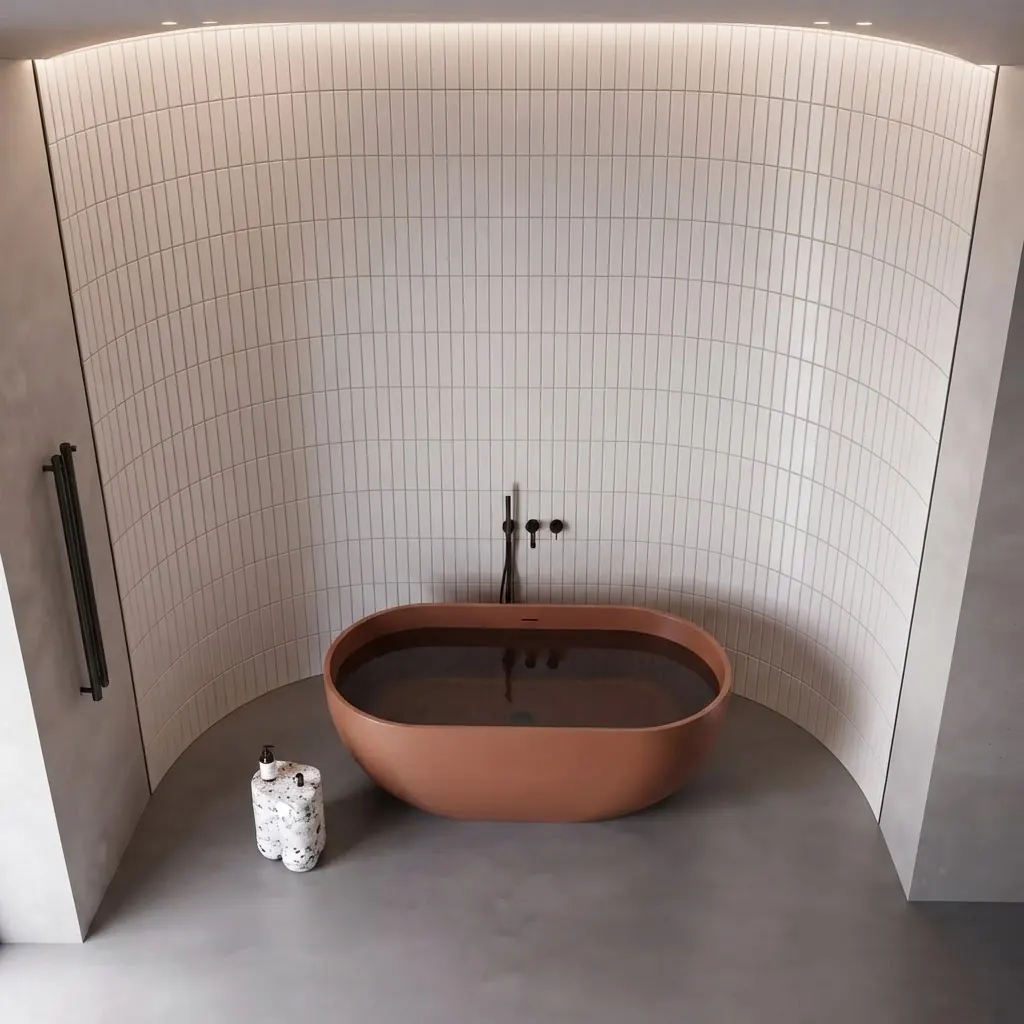 Terracotta colored oval freestanding bathtub against a curved white tiled wall with a slim floor mounted filler