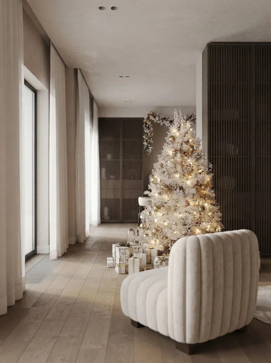 Hallway view into the same cream lounge with a white flocked Christmas tree glowing at the end of the corridor, wrapped gifts beneath it and a channel-tufted boucle armchair in the foreground
